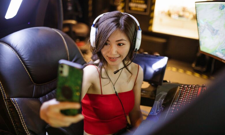 A young woman gamer with headphones taking a selfie during a gaming session.