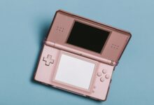 Close-up of a pink portable gaming console with dual screens on a blue surface.