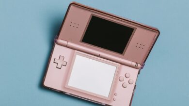 Close-up of a pink portable gaming console with dual screens on a blue surface.