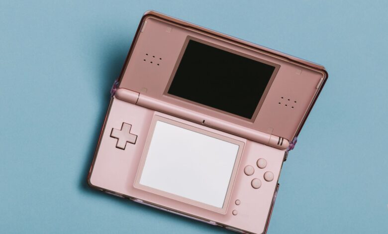 Close-up of a pink portable gaming console with dual screens on a blue surface.