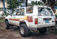 Old Toyota SUV covered in colorful stickers and parked outside in a casual urban setting.