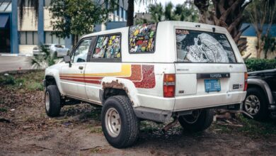 Old Toyota SUV covered in colorful stickers and parked outside in a casual urban setting.