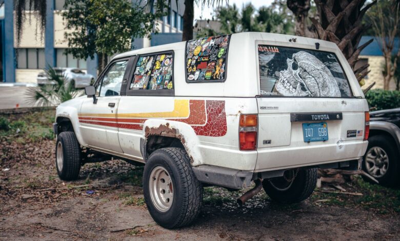 Old Toyota SUV covered in colorful stickers and parked outside in a casual urban setting.