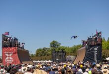 A skateboarder launches off a ramp in mid-air during a vibrant X Games event.