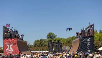 A skateboarder launches off a ramp in mid-air during a vibrant X Games event.