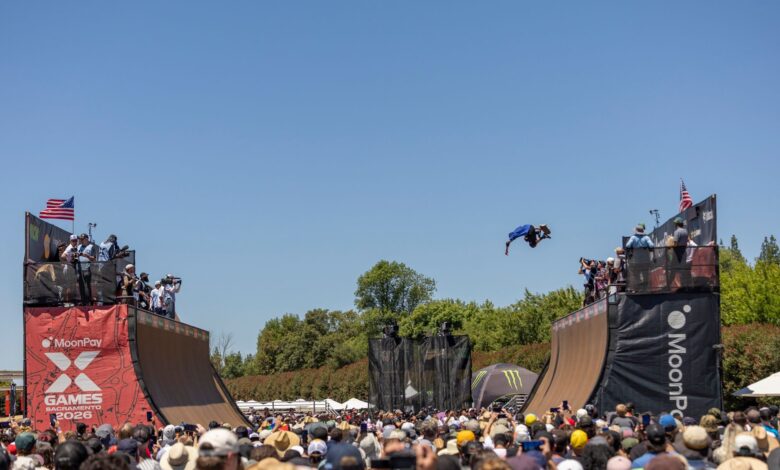 A skateboarder launches off a ramp in mid-air during a vibrant X Games event.