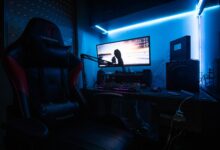 A sleek gaming desk with a monitor, gaming chair, and LED lights creating an immersive environment.