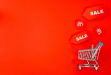 Shopping cart with sale tags on vibrant red backdrop promoting discounts.