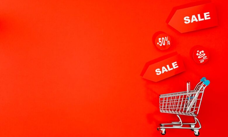 Shopping cart with sale tags on vibrant red backdrop promoting discounts.