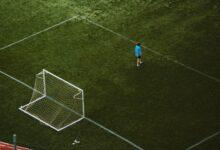 Aerial view of a lone soccer player near a goalpost on a grassy field.