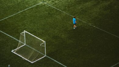 Aerial view of a lone soccer player near a goalpost on a grassy field.