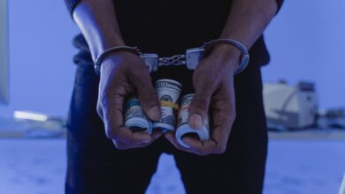 Close-up of handcuffed hands holding rolled cash, suggesting crime or arrest.