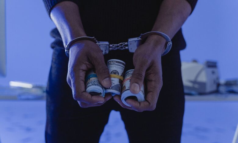 Close-up of handcuffed hands holding rolled cash, suggesting crime or arrest.