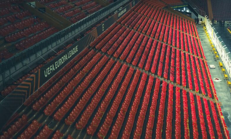 Rows of empty red seats in a UEFA Europa League stadium, captured from above.