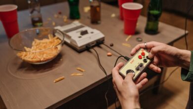 Hands holding a vintage game controller during a casual retro gaming night with snacks and drinks.