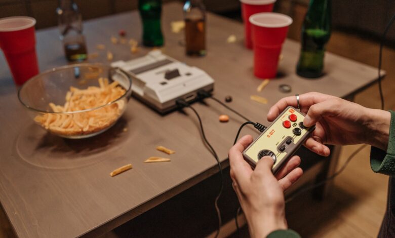 Hands holding a vintage game controller during a casual retro gaming night with snacks and drinks.