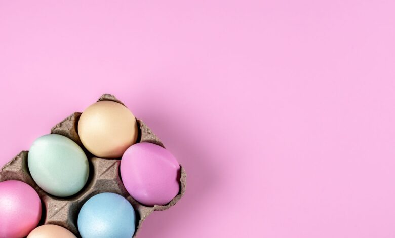 Pastel-colored Easter eggs in a carton on a pink background, perfect for spring themes.