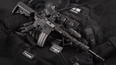 Close-up of tactical military gear including a rifle, radio, and vest on a dark background.