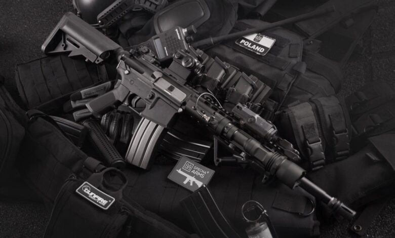 Close-up of tactical military gear including a rifle, radio, and vest on a dark background.