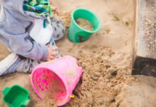 A child enjoys playing in a sandbox using vibrant colored buckets during a sunny day.
