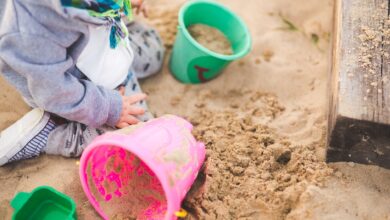 A child enjoys playing in a sandbox using vibrant colored buckets during a sunny day.