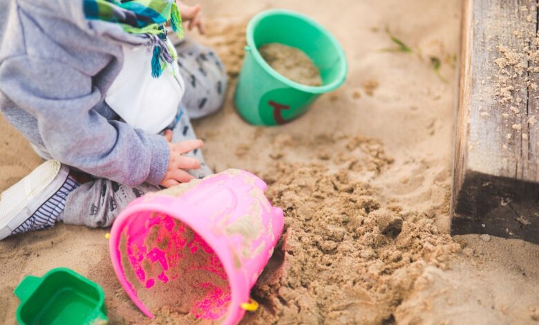A child enjoys playing in a sandbox using vibrant colored buckets during a sunny day.