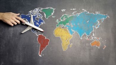 Top view of crop anonymous person holding toy airplane on colorful world map drawn on chalkboard
