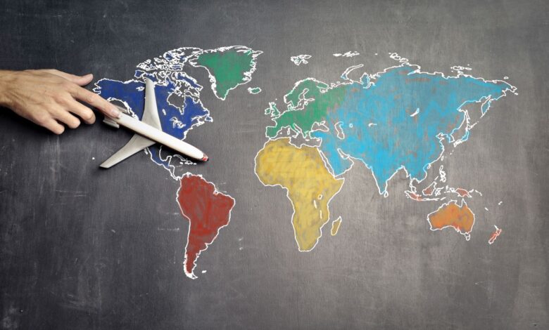 Top view of crop anonymous person holding toy airplane on colorful world map drawn on chalkboard