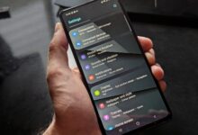 Hand holding smartphone displaying settings screen with various options evident.