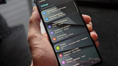 Hand holding smartphone displaying settings screen with various options evident.