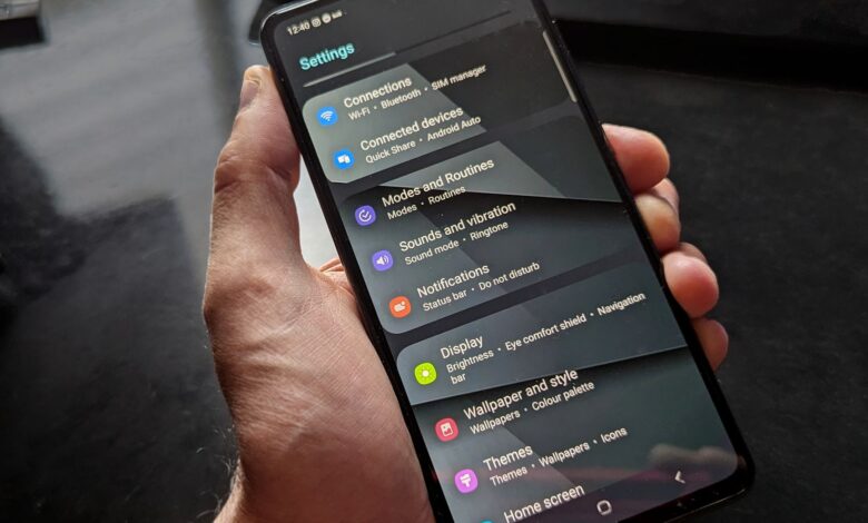 Hand holding smartphone displaying settings screen with various options evident.