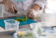 A chef expertly chops fresh herbs on a blue cutting board in a professional kitchen environment.