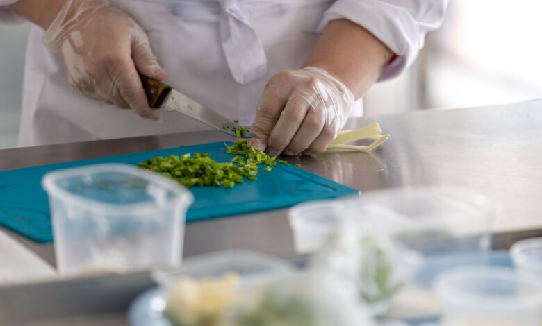 A chef expertly chops fresh herbs on a blue cutting board in a professional kitchen environment.