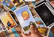 A person holds tarot cards in a colorful setting, showcasing divination tools and symbols.