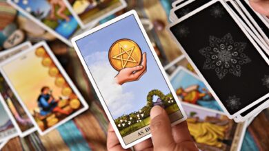 A person holds tarot cards in a colorful setting, showcasing divination tools and symbols.