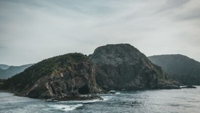 Dramatic coastal rock formation with ocean waves and a cloudy sky creating a moody seascape.