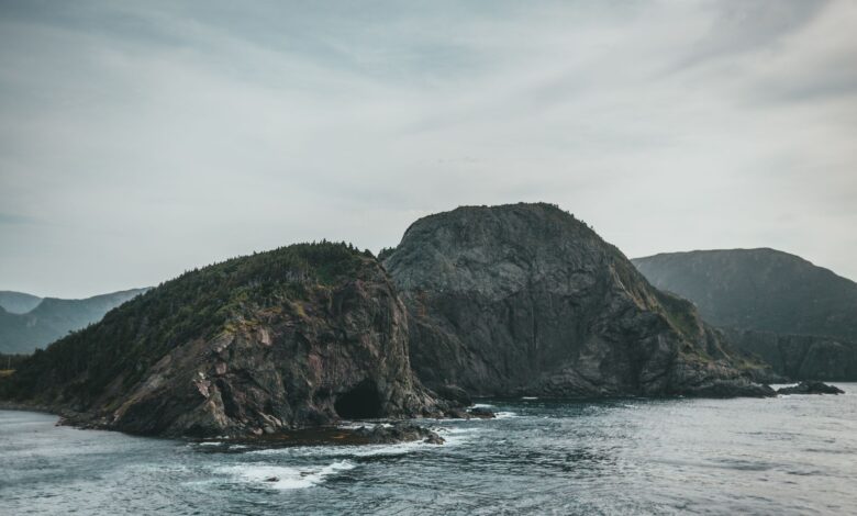 Dramatic coastal rock formation with ocean waves and a cloudy sky creating a moody seascape.