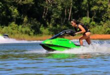 A woman rides a green jet ski at high speed on a sunny day, showcasing excitement and fun.