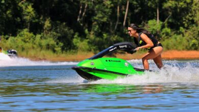 A woman rides a green jet ski at high speed on a sunny day, showcasing excitement and fun.