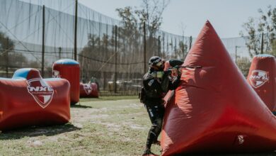 Paintball player strategizing behind inflatable cover during a competition on an outdoor field.