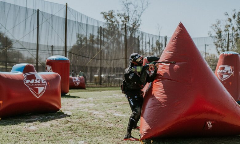 Paintball player strategizing behind inflatable cover during a competition on an outdoor field.