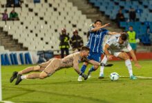 Dramatic soccer scene with goalkeeper diving to stop two players in a competitive match.