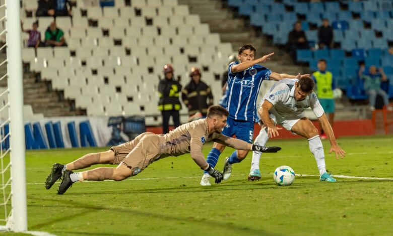 Dramatic soccer scene with goalkeeper diving to stop two players in a competitive match.