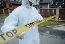 A person wearing a protective suit, handling yellow tape with 'STOP' in an outdoor urban setting.
