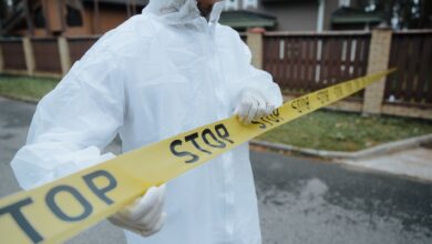 A person wearing a protective suit, handling yellow tape with 'STOP' in an outdoor urban setting.