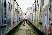 Man jumps between two graffiti-covered trains, expressing joy and freedom.