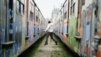 Man jumps between two graffiti-covered trains, expressing joy and freedom.
