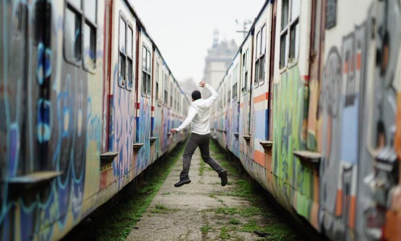 Man jumps between two graffiti-covered trains, expressing joy and freedom.