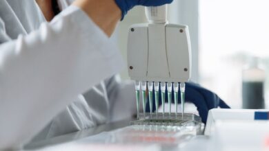 A scientist wearing a lab coat uses a multichannel pipette for liquid handling in a lab setting.