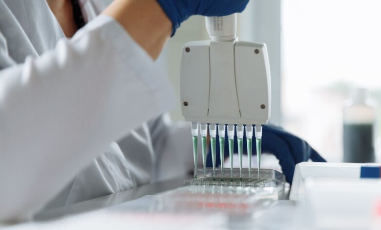 A scientist wearing a lab coat uses a multichannel pipette for liquid handling in a lab setting.